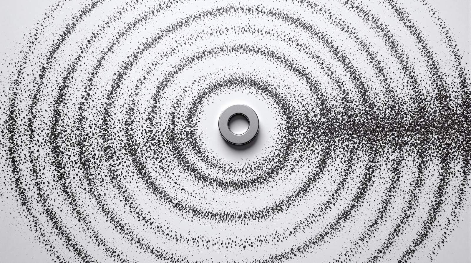 Iron filings on white paper arranged in curving rings around a small magnet