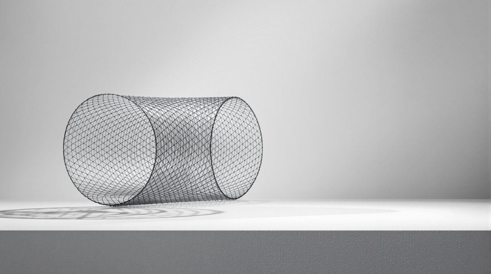 A sculptural cylinder of rolled fine hexagonal steel mesh lying on a pale grey surface